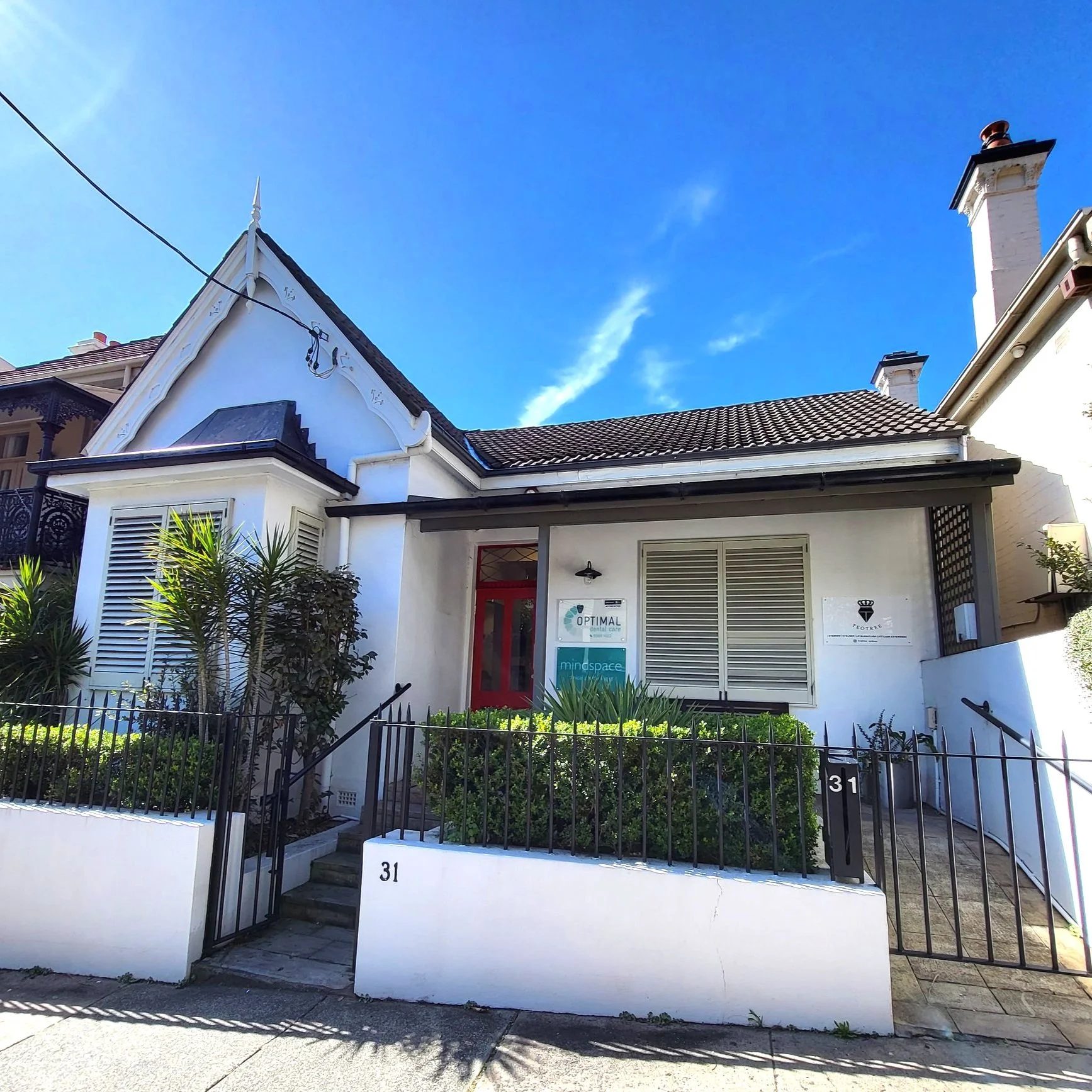 The exterior of the Optimal Dental Care practice — a white heritage cottage at 31 Grosvenor Street, Woollahra, with the Optimal Dental Care sign by the red front door