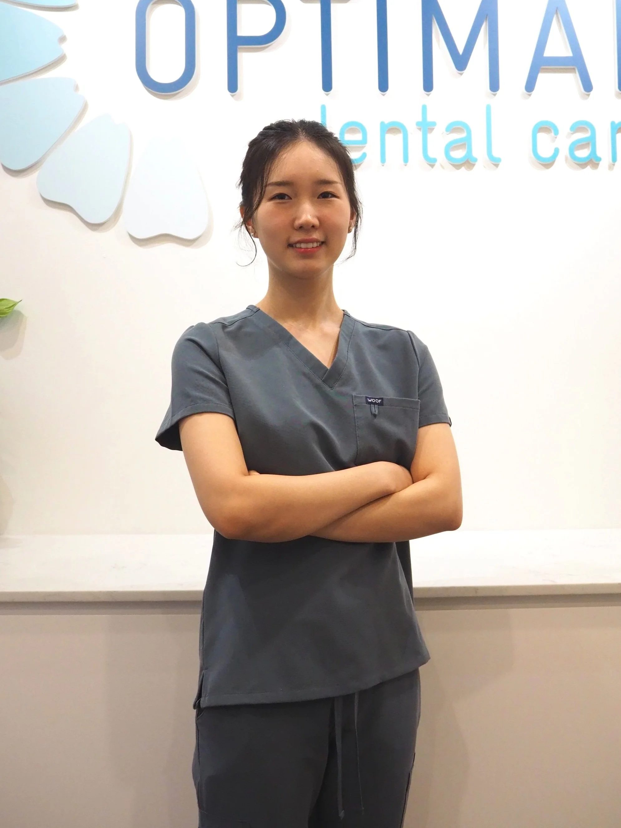 Dr Kate Lee, Associate Dentist at Optimal Dental Care, in front of the practice wall logo