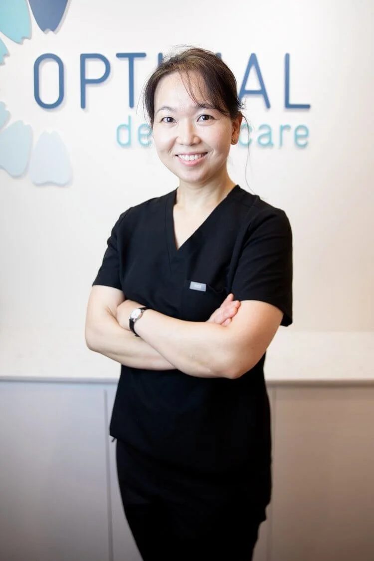 Dr Anna Lee, Principal Dentist at Optimal Dental Care, in front of the practice wall logo
