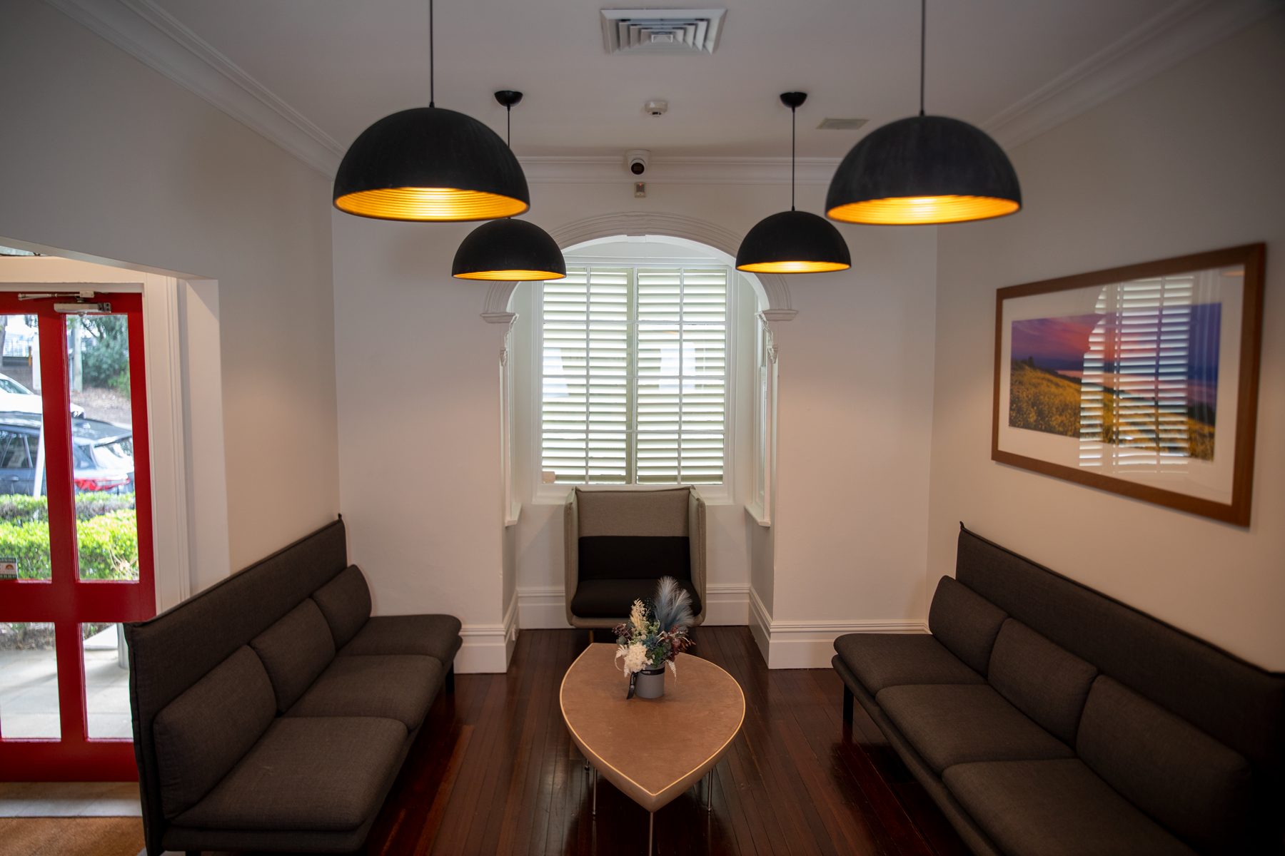 The reception and waiting area at Optimal Dental Care, with timber floors, dome pendant lights and framed coastal artwork