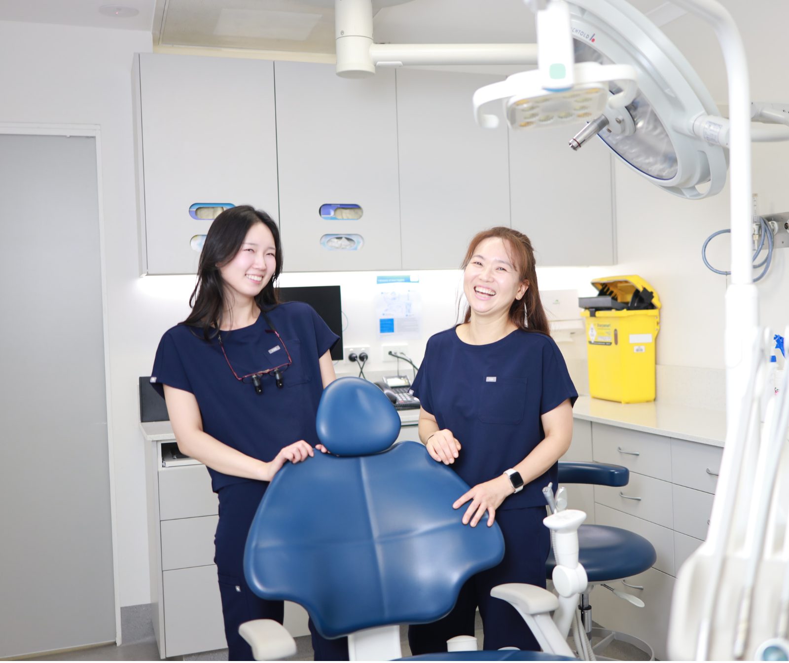 Two Optimal Dental Care clinicians smiling beside a treatment chair